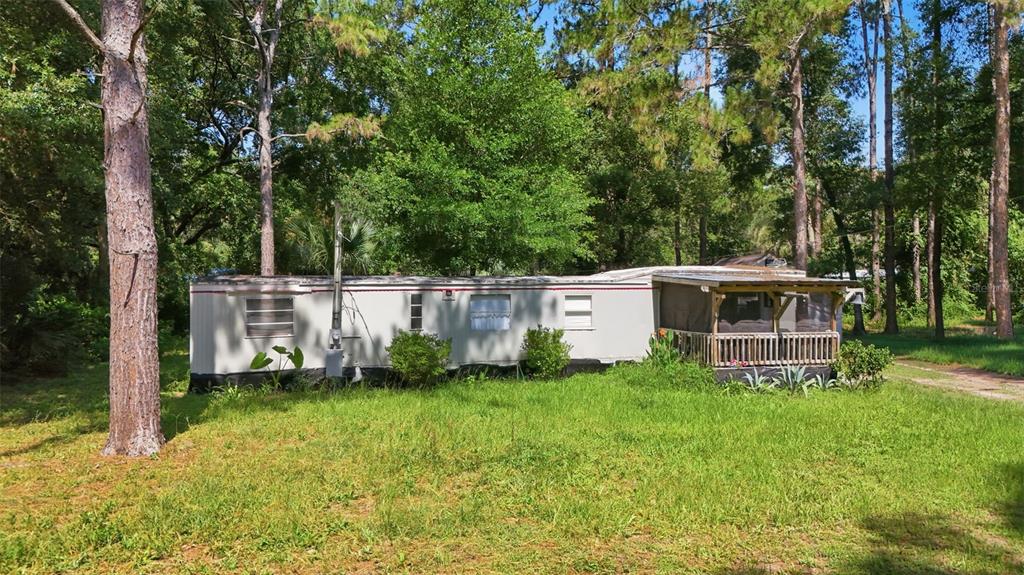 A single-wide mobile home with a screened-in porch sits on a grassy, wooded lot — 43025 E 3RD STREET, PAISLEY, FL