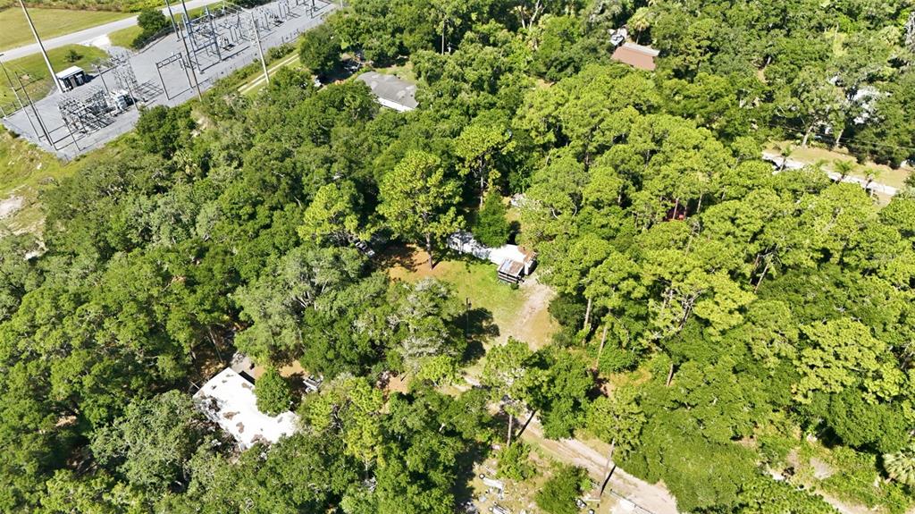 An aerial view shows a wooded lot with two small structures and a nearby substation — 43025 E 3RD STREET, PAISLEY, FL