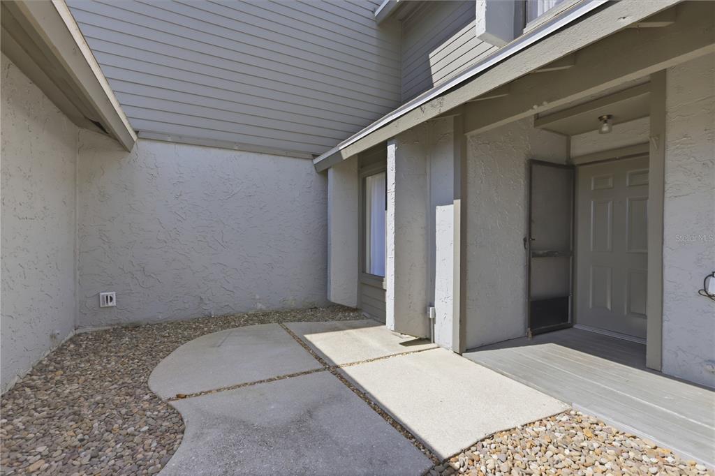 A concrete patio sits in front of a house entrance with gray siding and stucco — 130 LIMEWOOD PLACE UNIT 3, ORMOND BEACH, FL