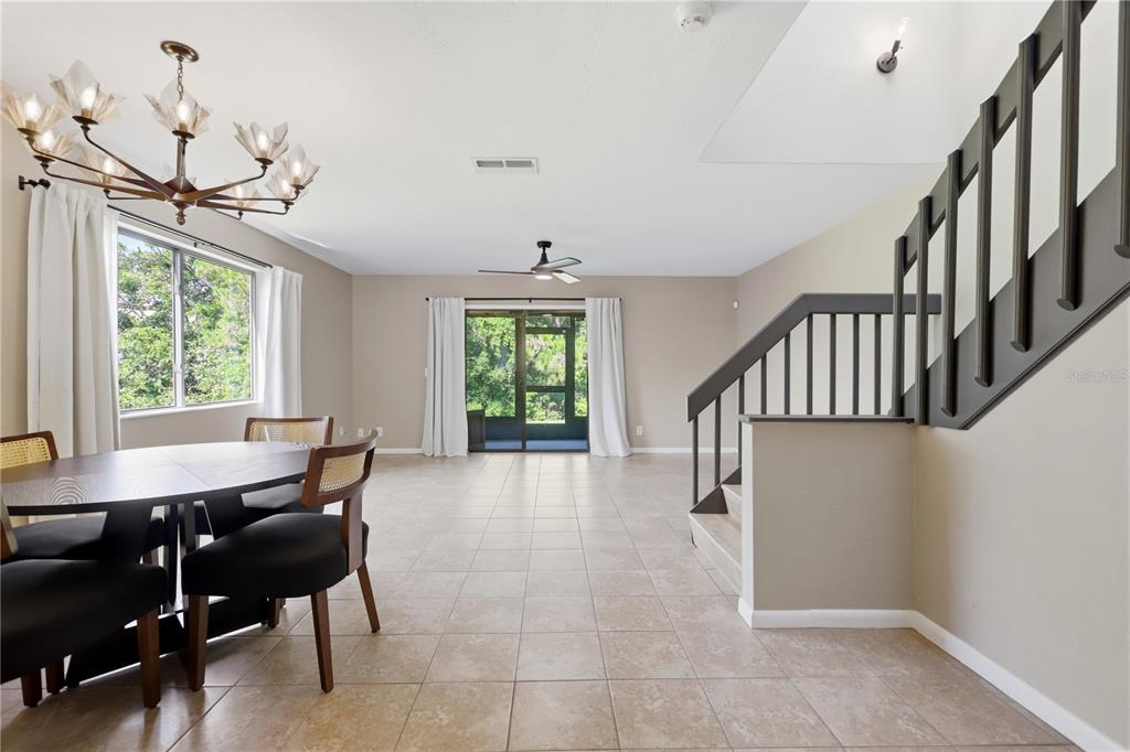 A dining area with a chandelier and tile flooring leads to a staircase and patio — 130 LIMEWOOD PLACE UNIT 3, ORMOND BEACH, FL