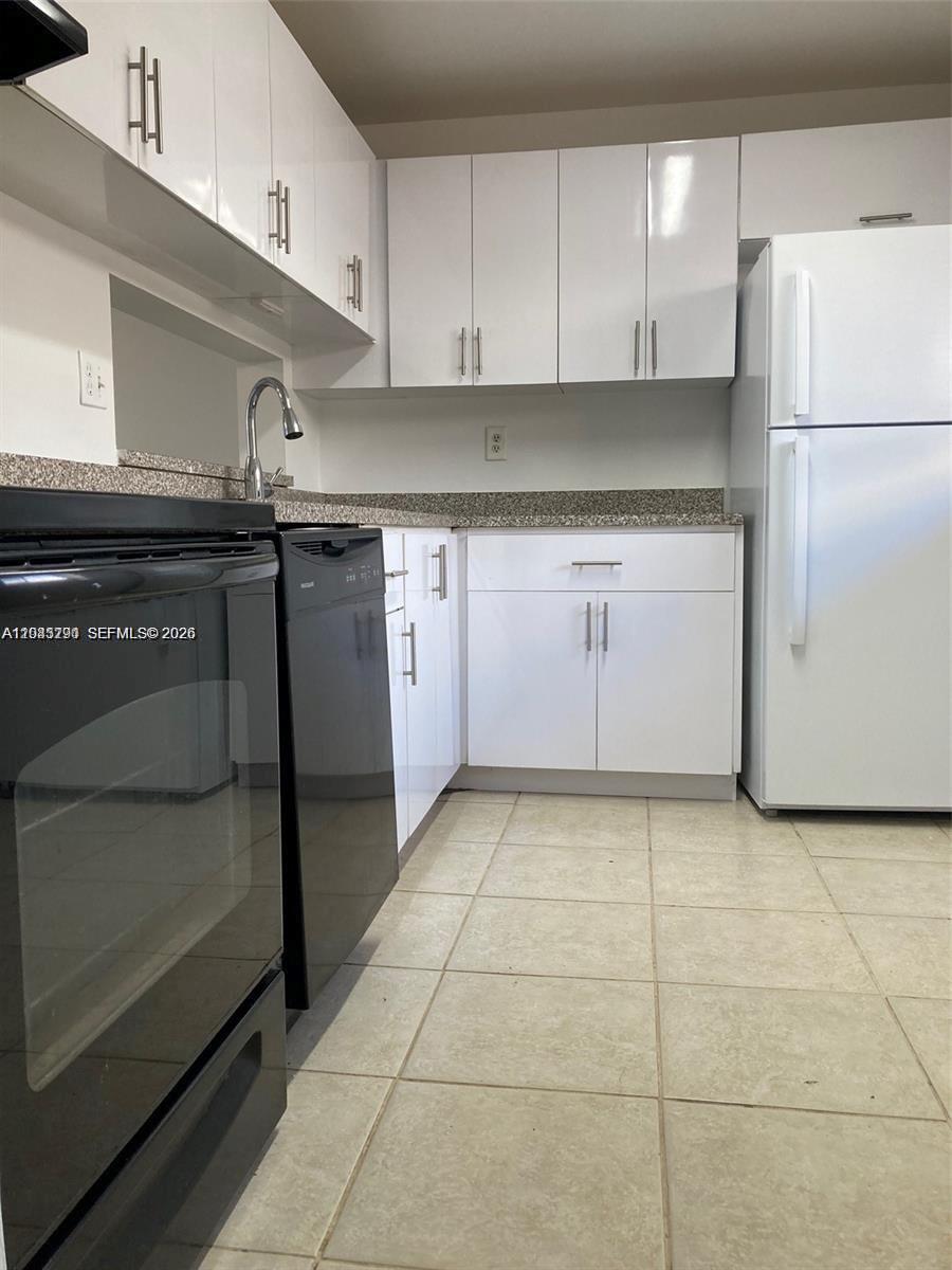 A kitchen features white cabinets, a speckled countertop, and black appliances on a tiled floor — 8420 SW 133rd Ave Rd # 422, Miami FL 33183, MIAMI, FL
