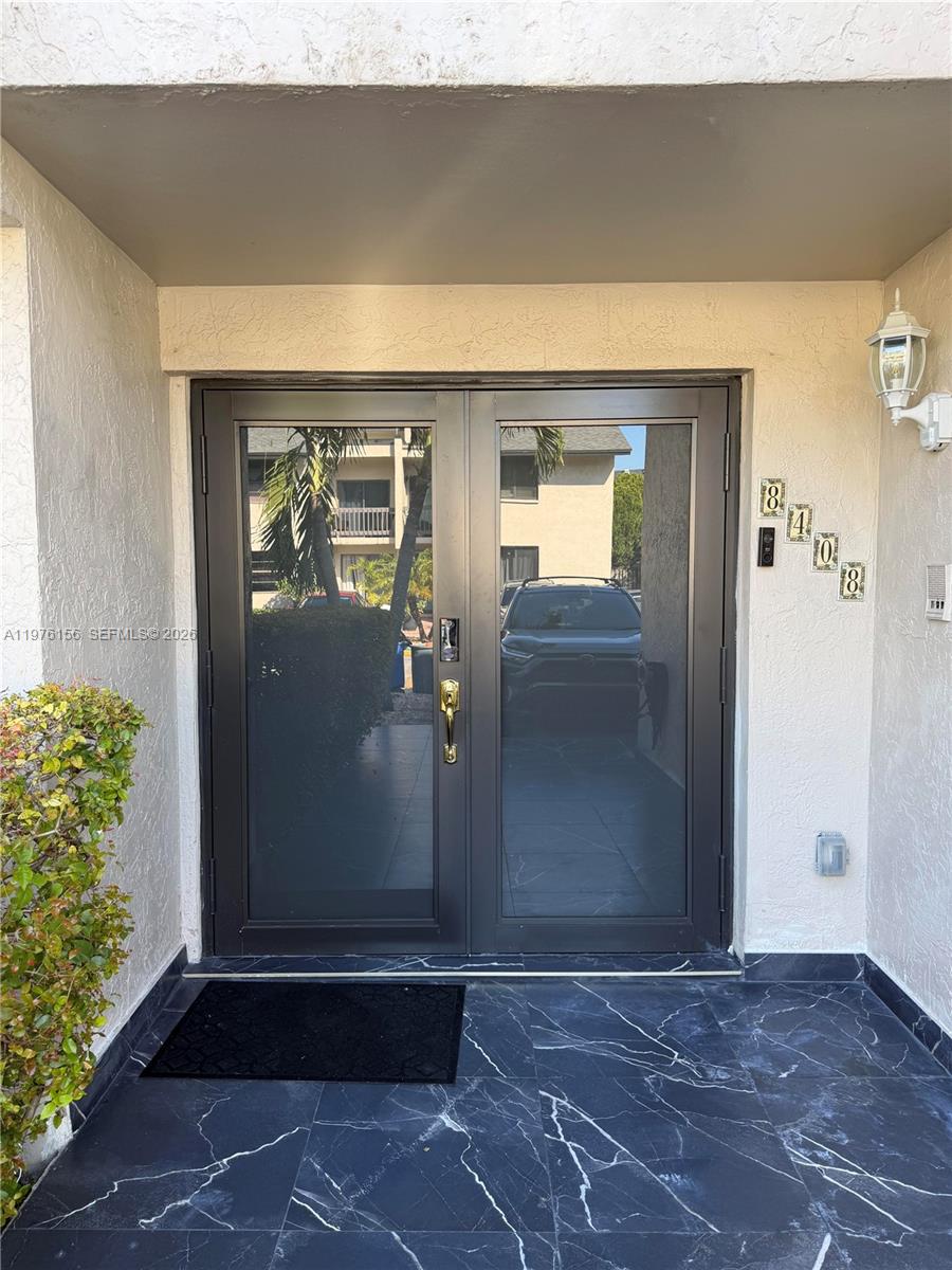 A set of dark-framed glass double doors opens onto a black marble-tiled entryway — 8408 NW 8th St # 8408, Miami FL 33126, MIAMI, FL