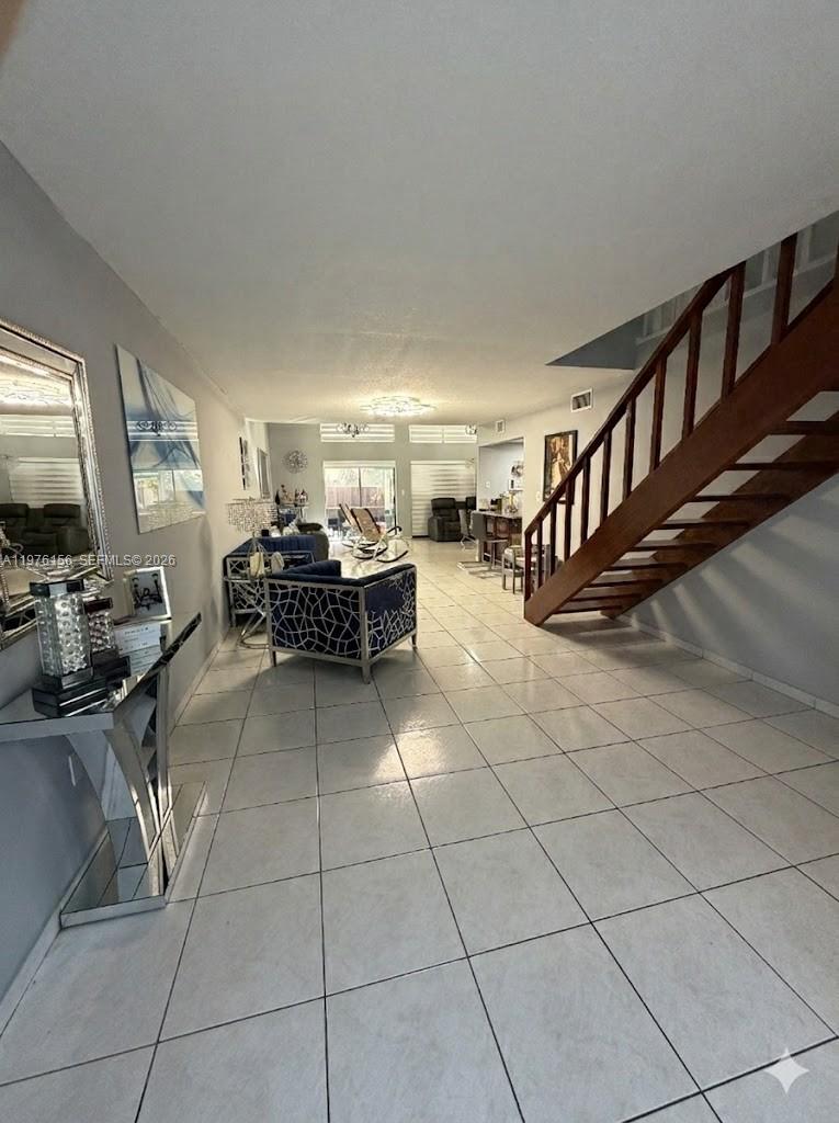 A tiled living room features a wooden staircase and a modern blue patterned armchair — 8408 NW 8th St # 8408, Miami FL 33126, MIAMI, FL