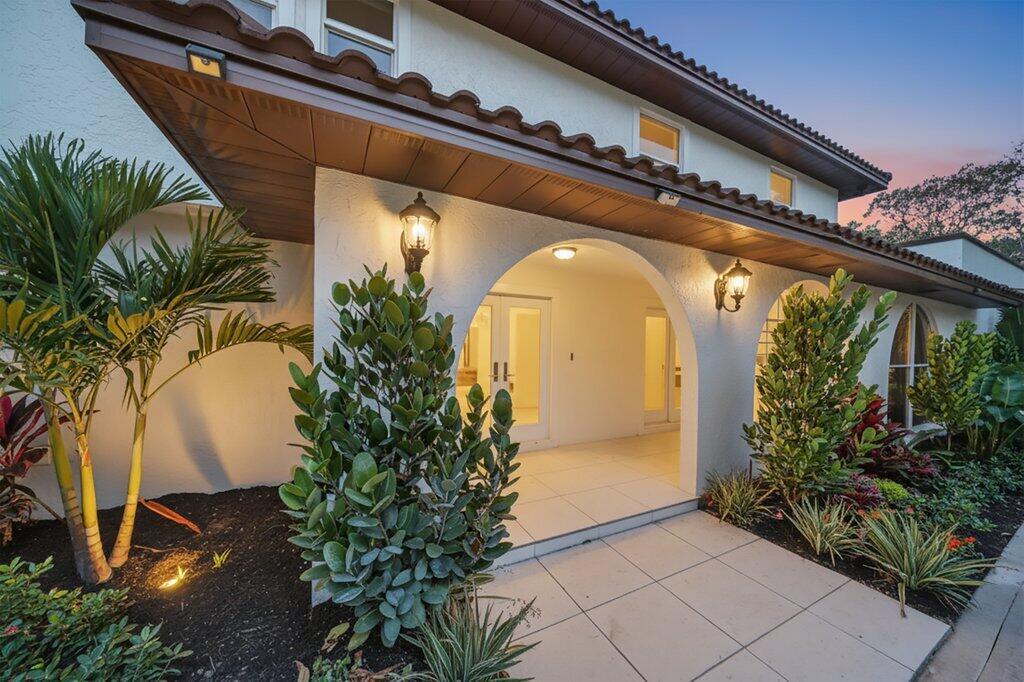 The exterior of a white house features arched entryways, tiled flooring, and landscaped garden beds — 37 E High Point Road, Sewalls Point FL 34996, SEWALLS POINT, FL