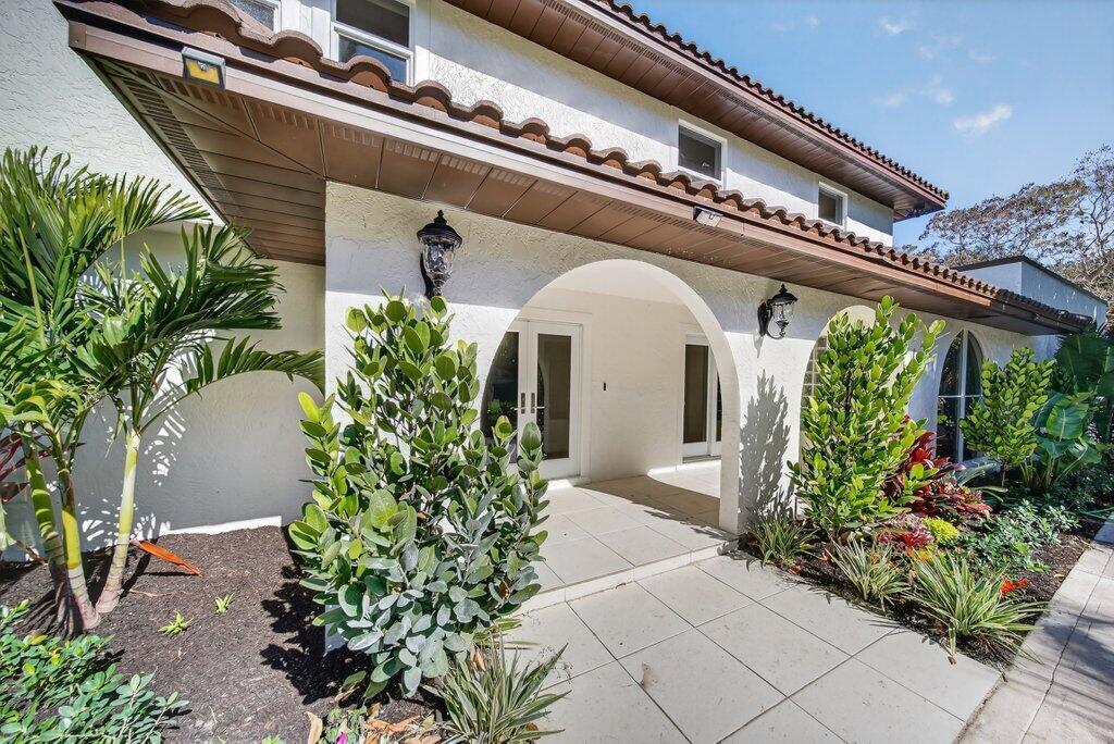The exterior of a white house features a covered entryway with arched openings and landscaping — 37 E High Point Road, Sewalls Point FL 34996, SEWALLS POINT, FL