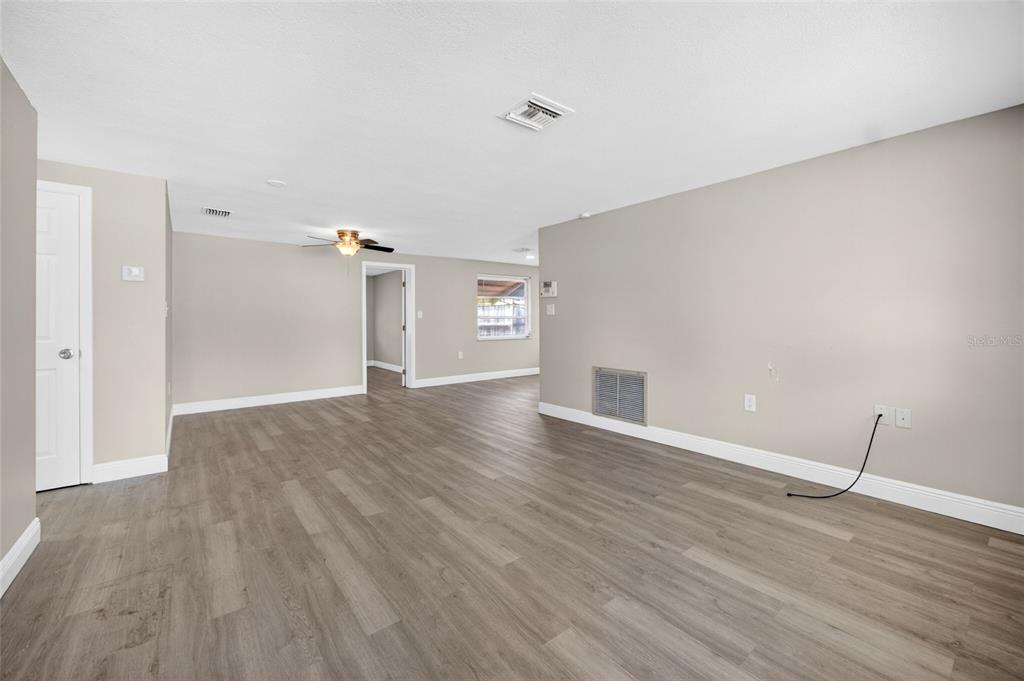An empty living room features light gray walls, wood-look flooring, and a ceiling fan — 10735 DARIUS STREET, PORT RICHEY, FL