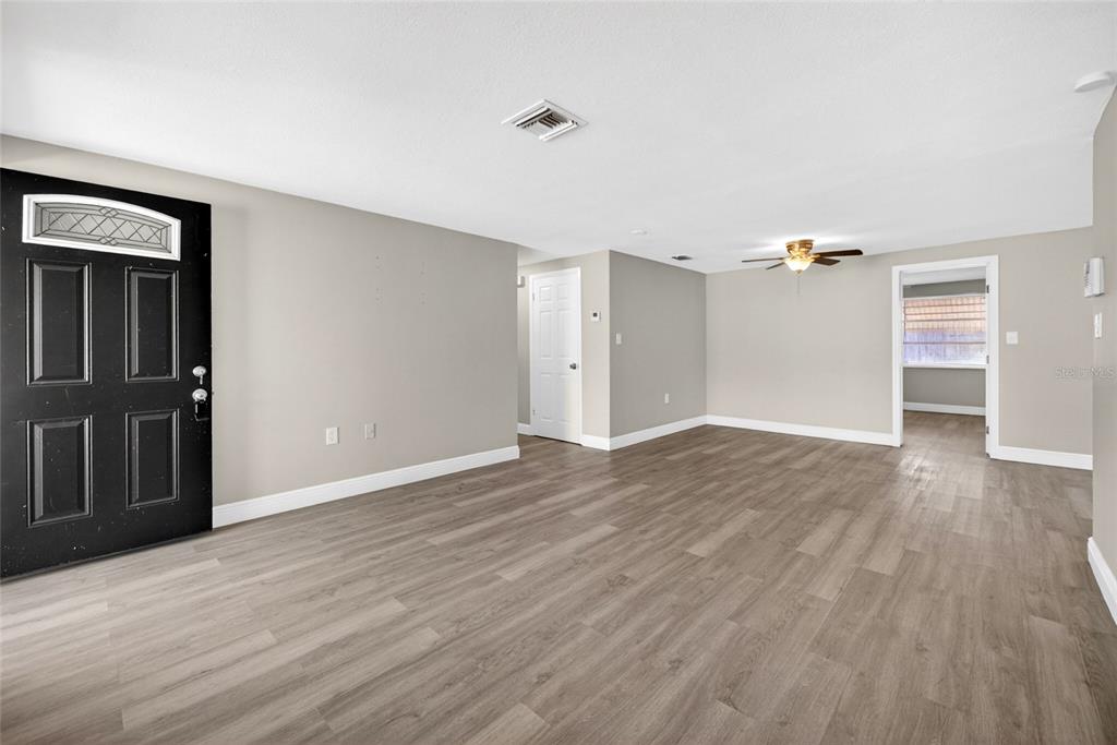 An empty living room features gray walls, wood-look flooring, a black front door, and ceiling fan — 10735 DARIUS STREET, PORT RICHEY, FL