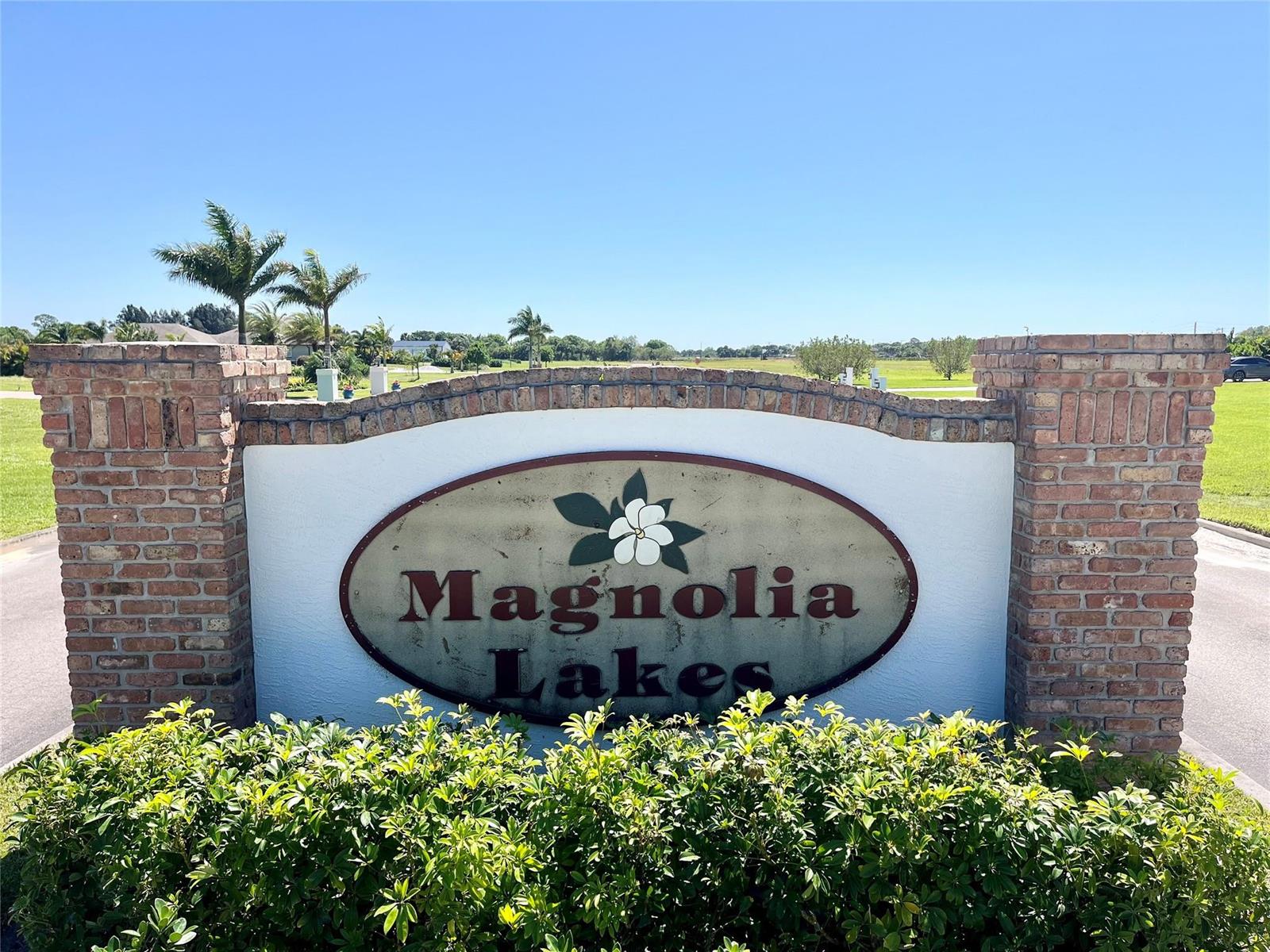 A brick-columned entrance sign for Magnolia Lakes stands in front of a grassy field — 555 65th Avenue, Vero Beach FL 32968, VERO BEACH, FL