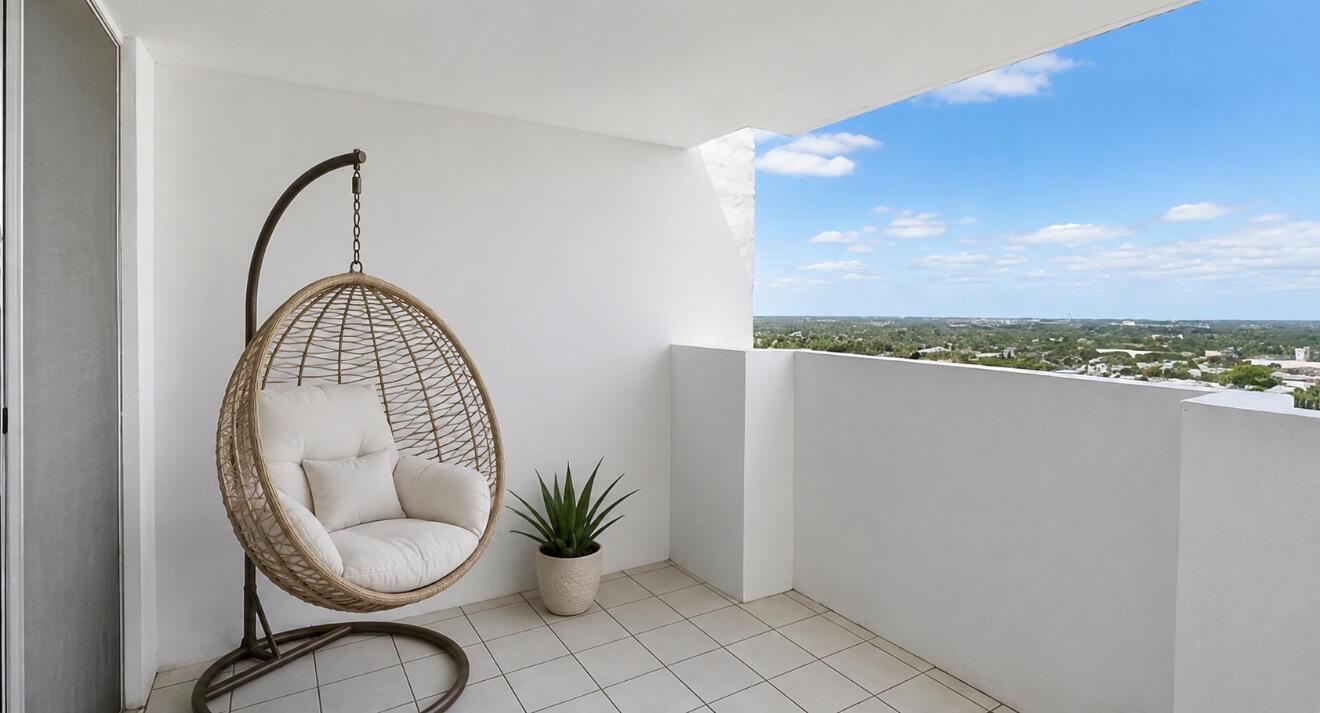 A balcony with white walls, tiled flooring, a hanging wicker chair, and a distant view — 2750 NE 183rd Street Ph, Aventura FL 33160, AVENTURA, FL