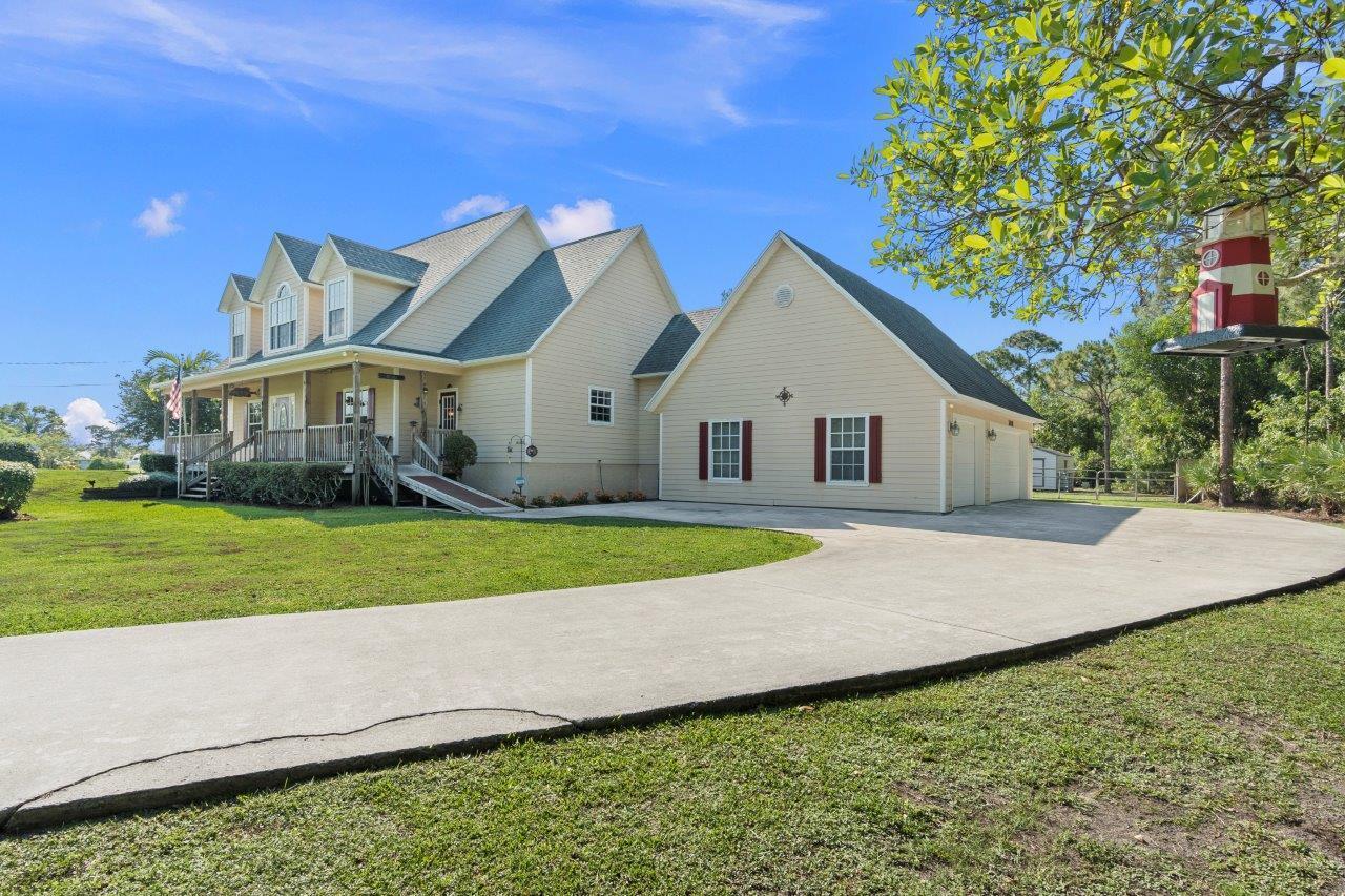 A two-story beige house with a wrap-around porch and an attached garage sits on grass — 405 SE Salerno Road, Stuart FL 34997, STUART, FL