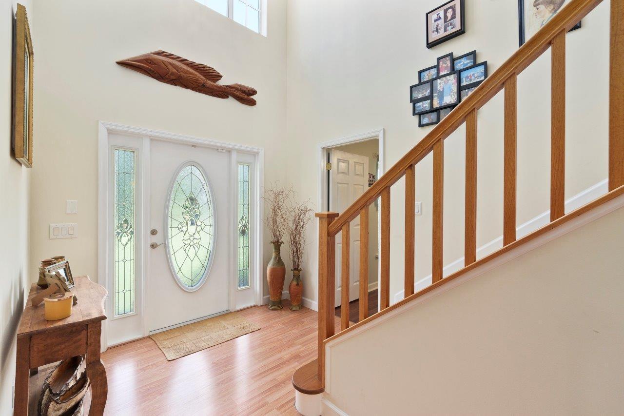 A bright entryway features a wooden staircase, a white front door, and light wood flooring — 405 SE Salerno Road, Stuart FL 34997, STUART, FL