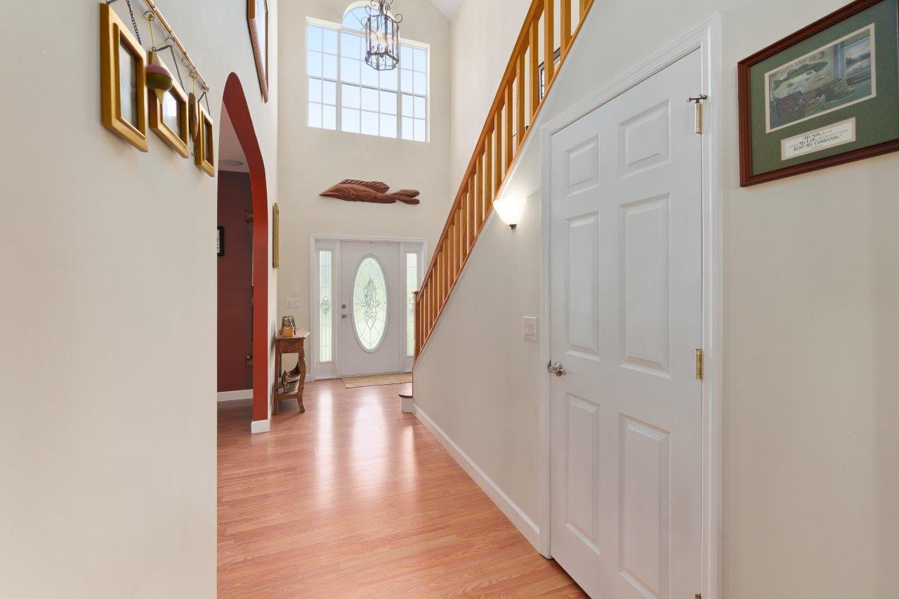 A bright entryway features a staircase with wooden railings, light wood flooring, and a front door — 405 SE Salerno Road, Stuart FL 34997, STUART, FL