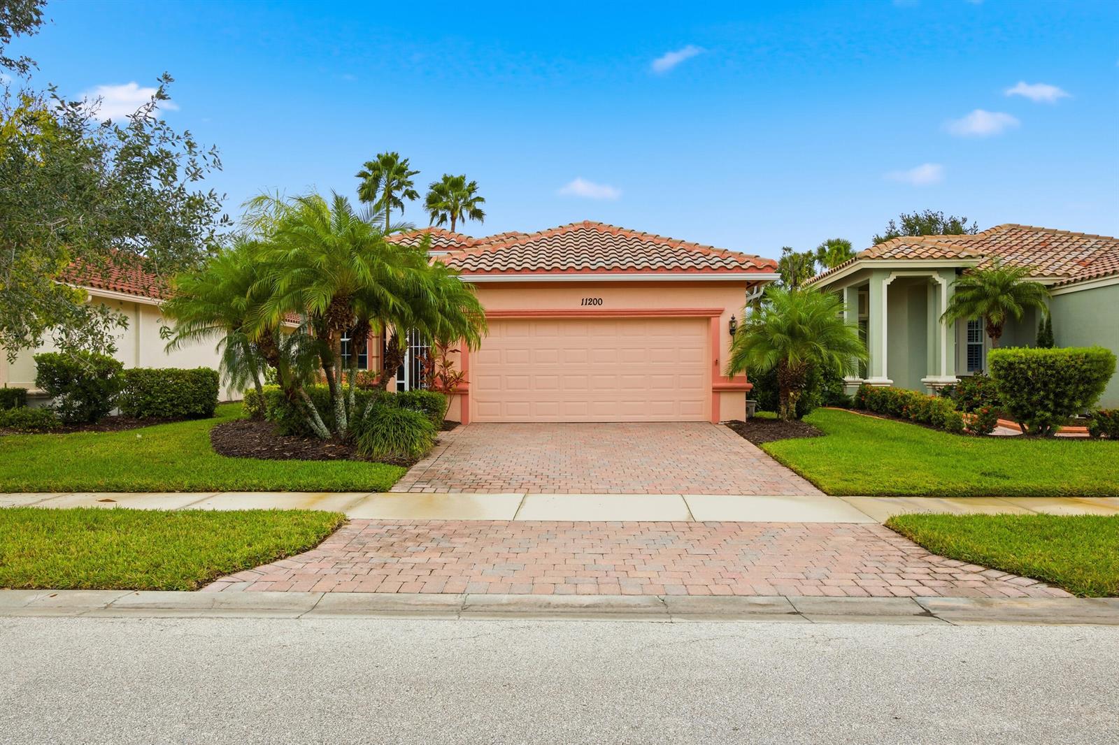 A single-story peach-colored house with a tiled roof, a two-car garage, and a paved driveway — 11200 SW Birch Tree Circle, Port St. Lucie FL 34987, PORT ST. LUCIE, FL