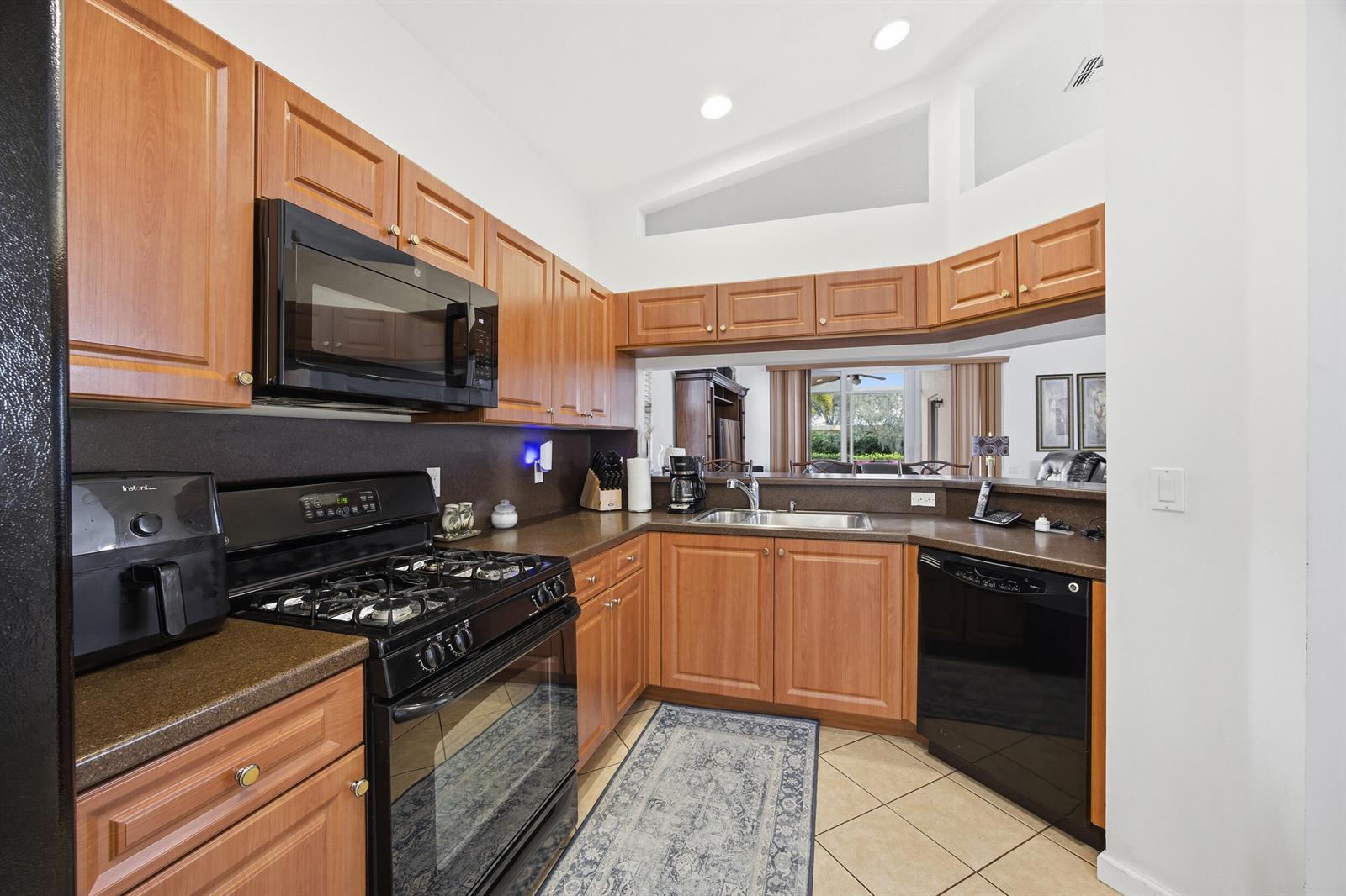 A kitchen features wood cabinets, dark countertops, black appliances, and a pass-through window — 11200 SW Birch Tree Circle, Port St. Lucie FL 34987, PORT ST. LUCIE, FL