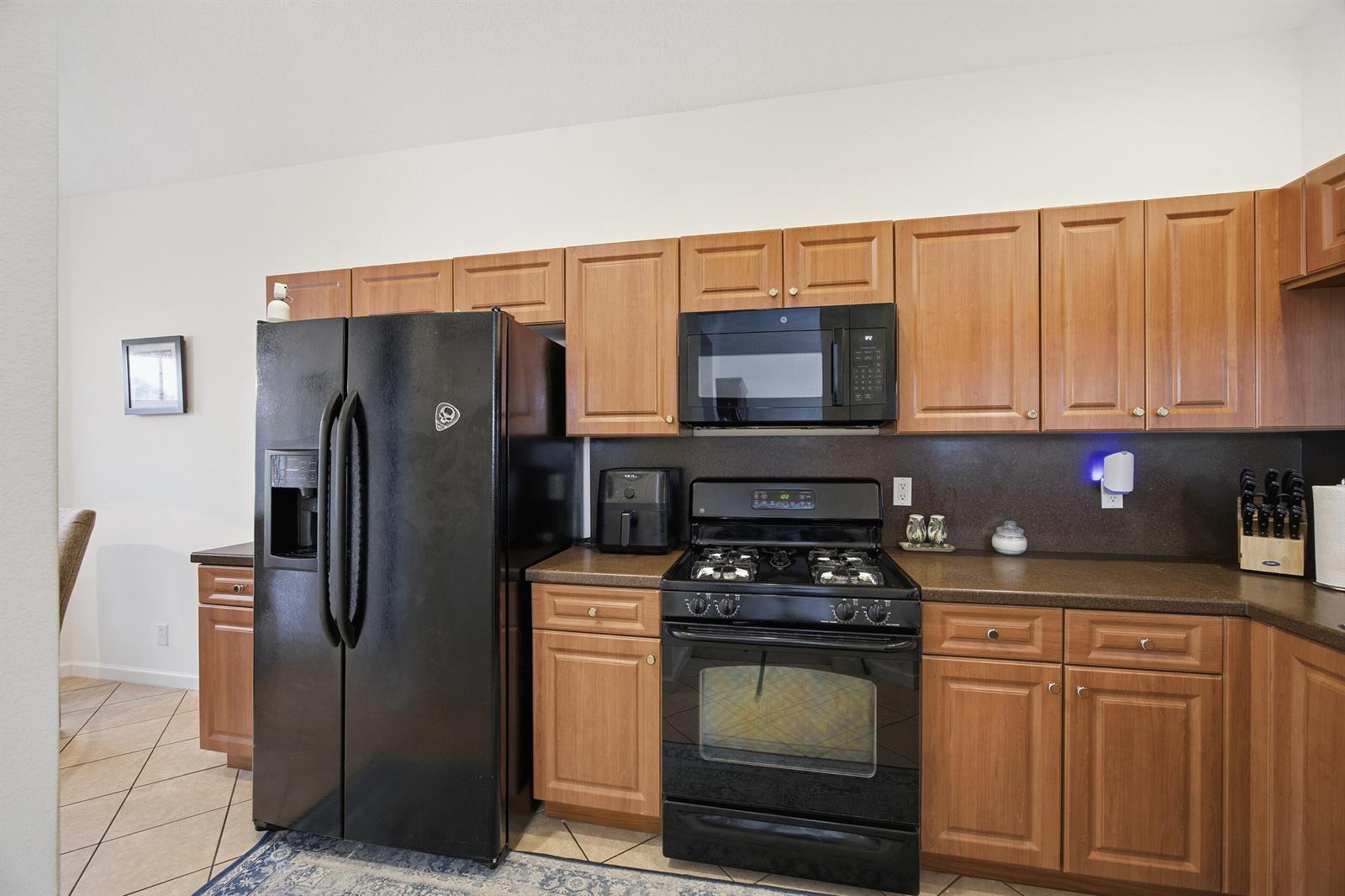 A kitchen features wood cabinets, black appliances, and dark countertops — 11200 SW Birch Tree Circle, Port St. Lucie FL 34987, PORT ST. LUCIE, FL