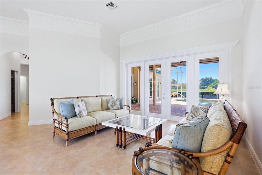 A living room with rattan furniture, tile floors, and glass doors opening to a pool — 7501 EATON COURT, UNIVERSITY PARK, FL