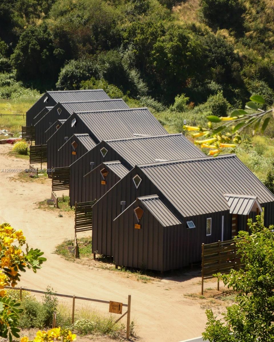 A row of identical dark-colored cabins with metal roofs sits along a dirt path — LODGE FOR SALE Santo Domigo (Chile), 2720000, FL