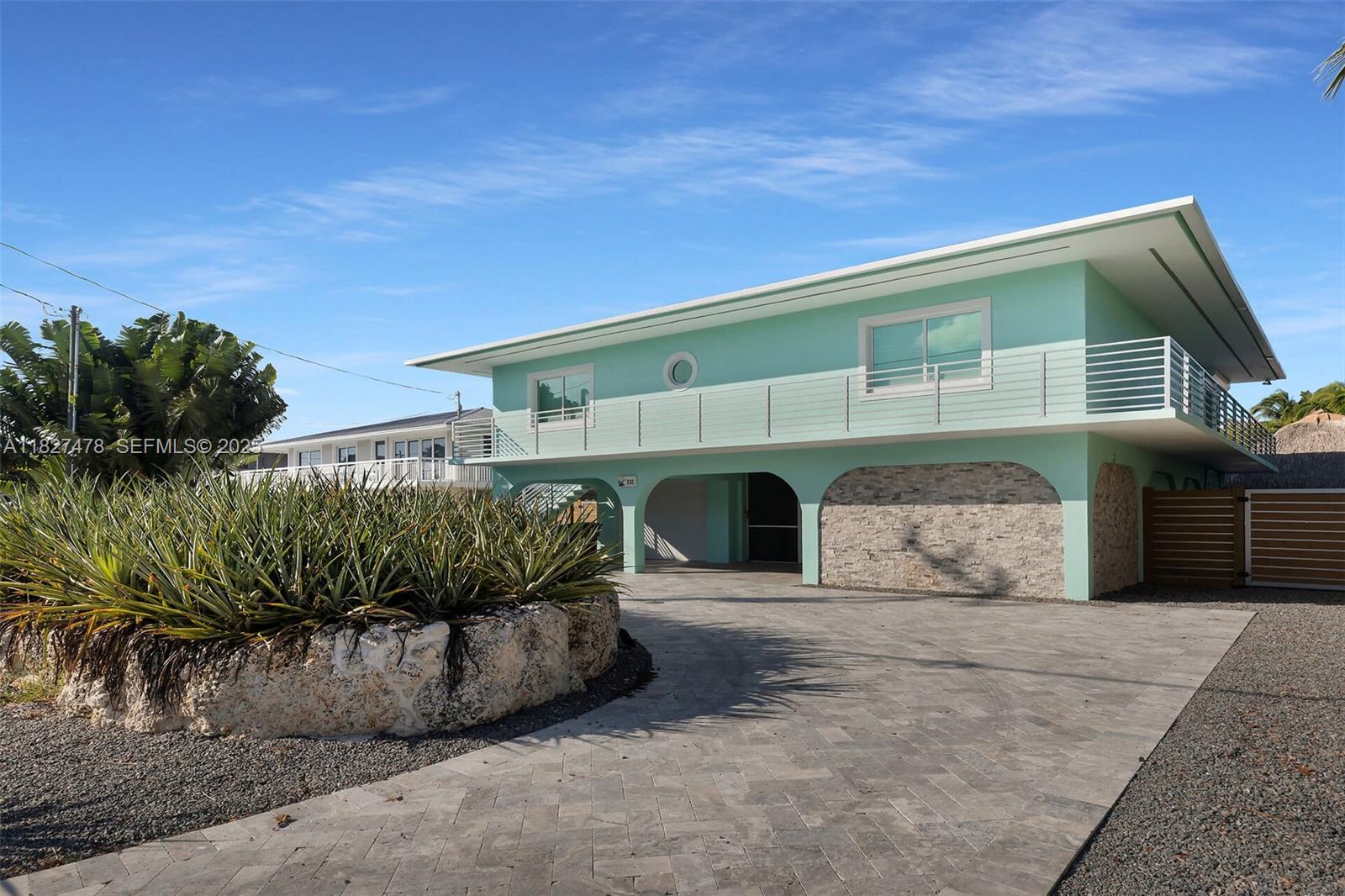 A two-story mint green house features a stone-clad ground floor, arched entryways, and a balcony — 232 W Seaview Dr, Duck FL 33050, DUCK, FL