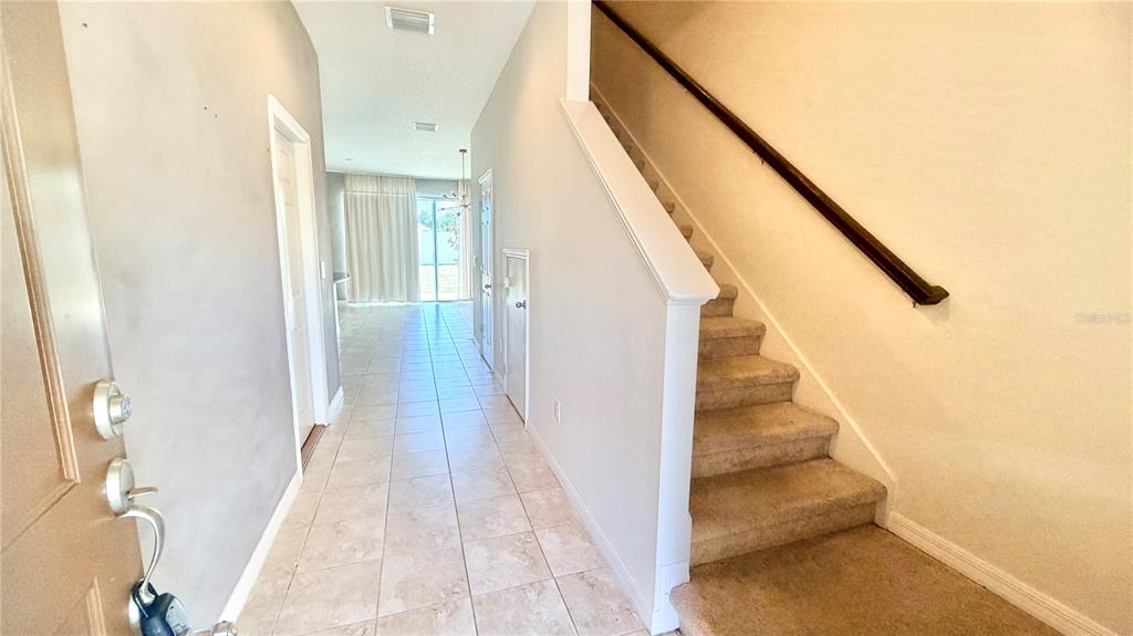 An entryway features tiled flooring, a carpeted staircase with a handrail, and a hallway ahead — 7037 WOODCHASE GLEN DRIVE, RIVERVIEW, FL