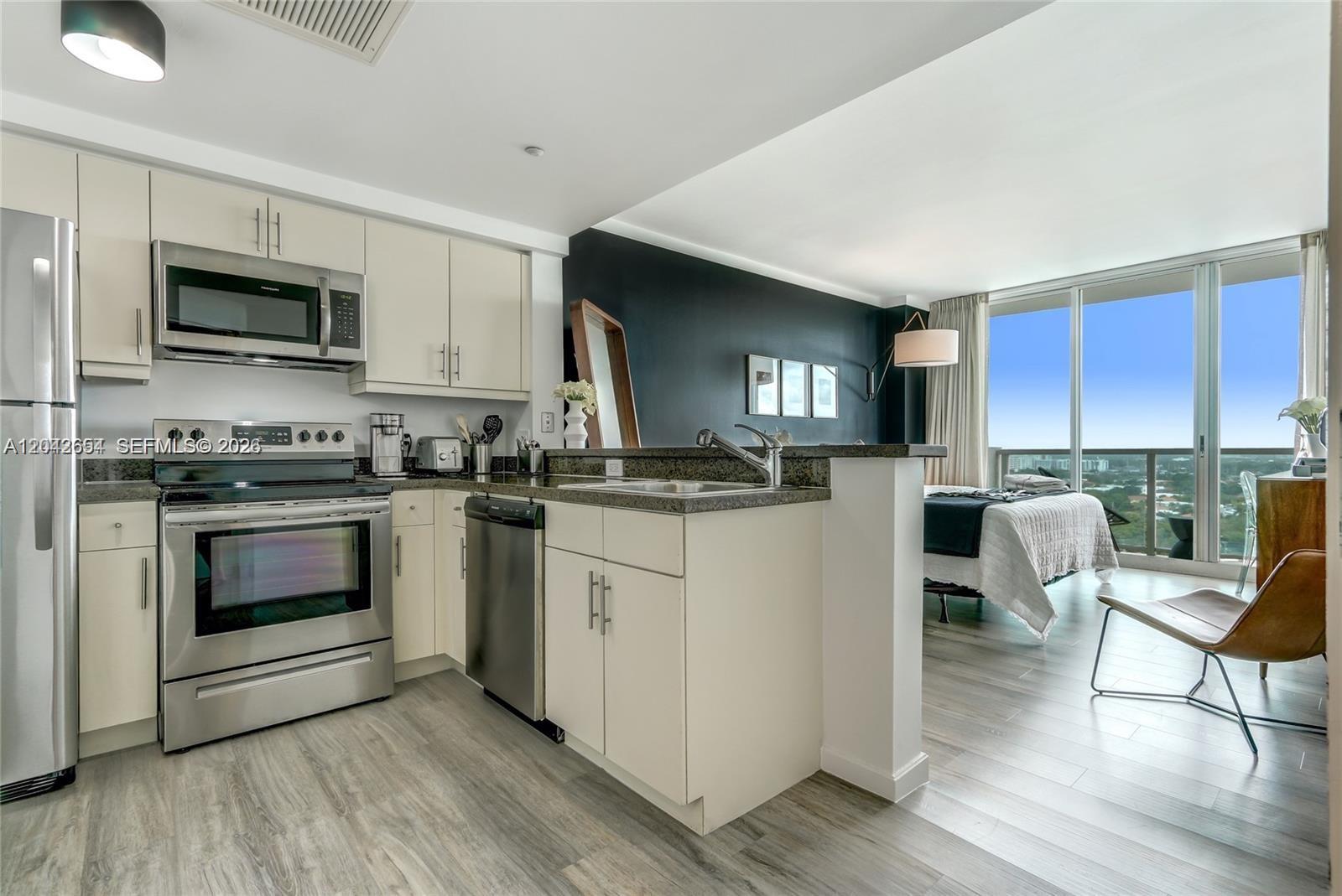 A kitchen with stainless steel appliances and cream cabinets overlooks a bedroom with balcony access — 2889 Mcfarlane Rd # 1811, Miami FL 33133, MIAMI, FL