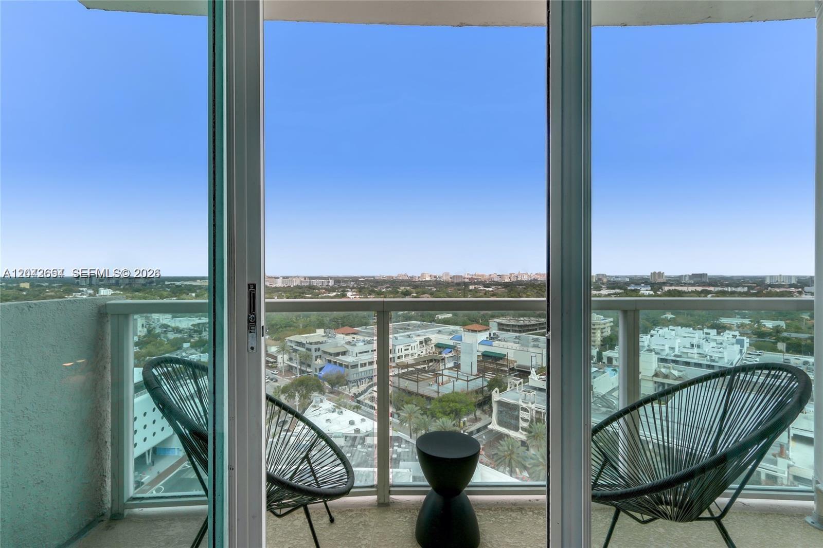 A balcony with two chairs and a small table overlooks a city and landscape — 2889 Mcfarlane Rd # 1811, Miami FL 33133, MIAMI, FL