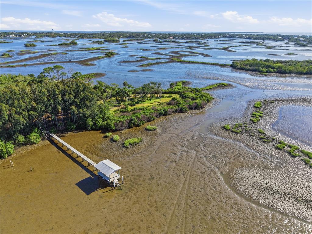 An aerial view shows a wooden dock extending into a tidal flat near coastal vegetation — 15780 SUNSET POINT DRIVE, CEDAR KEY, FL