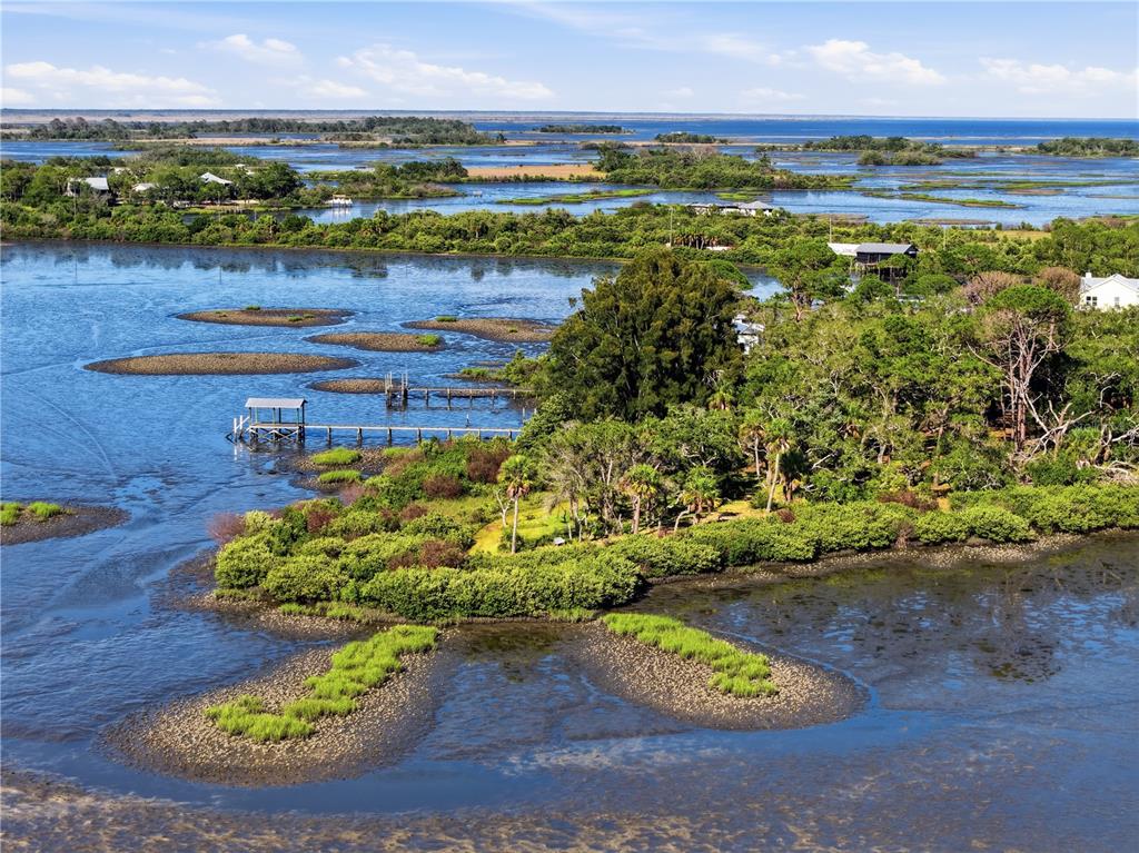 An aerial view of a coastal landscape featuring marshland, small islands, and a wooden dock — 15780 SUNSET POINT DRIVE, CEDAR KEY, FL