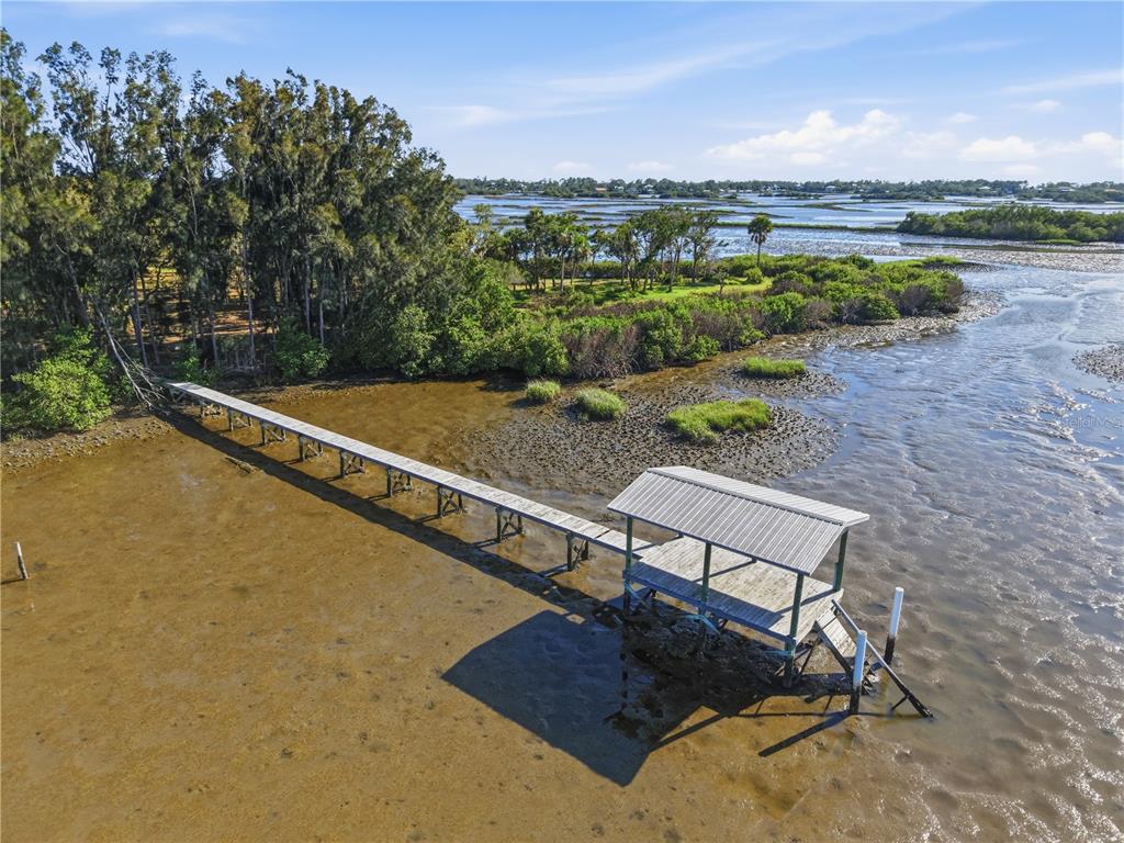 An aerial view shows a long wooden dock extending from a wooded shoreline over mudflats — 15780 SUNSET POINT DRIVE, CEDAR KEY, FL