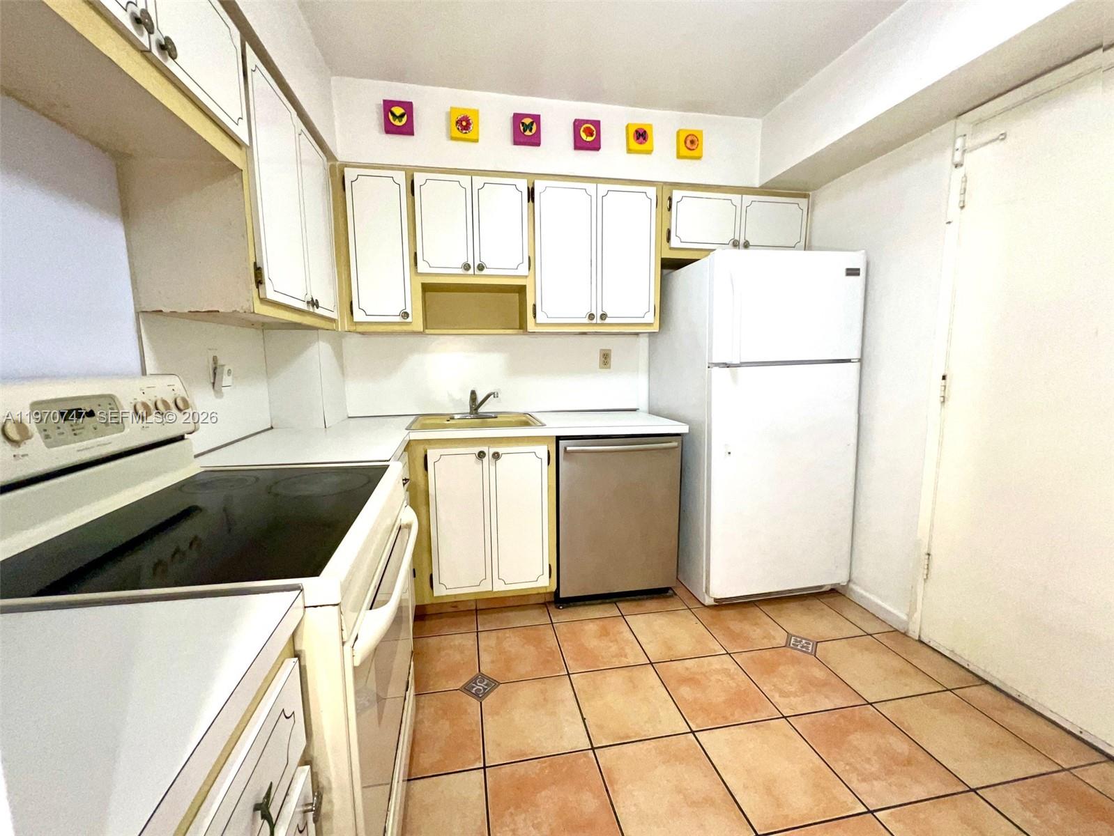 A kitchen features white cabinets with yellow trim, a white stove, and terracotta floor tiles — 1658 Bay Rd # 203, Miami Beach FL 33139, MIAMI BEACH, FL