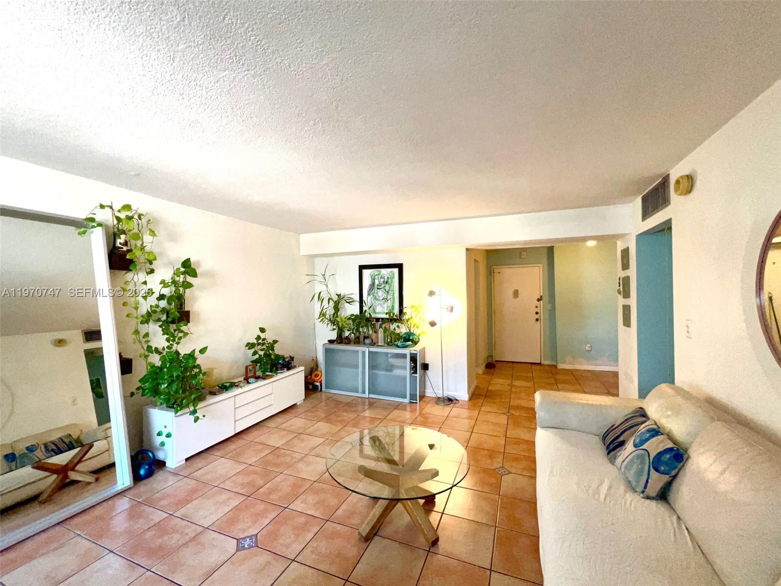 A living room features tile flooring, a glass coffee table, a white sofa, and plants — 1658 Bay Rd # 203, Miami Beach FL 33139, MIAMI BEACH, FL