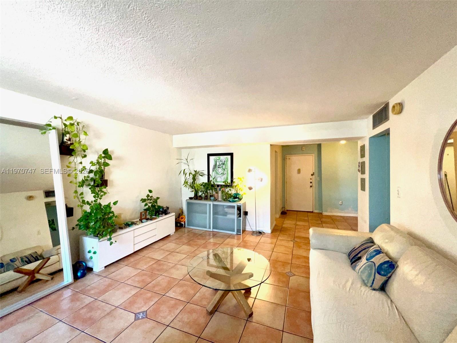 A living room features a white sofa, glass coffee table, tile flooring, and potted plants — 1658 Bay Rd # 203, Miami Beach FL 33139, MIAMI BEACH, FL