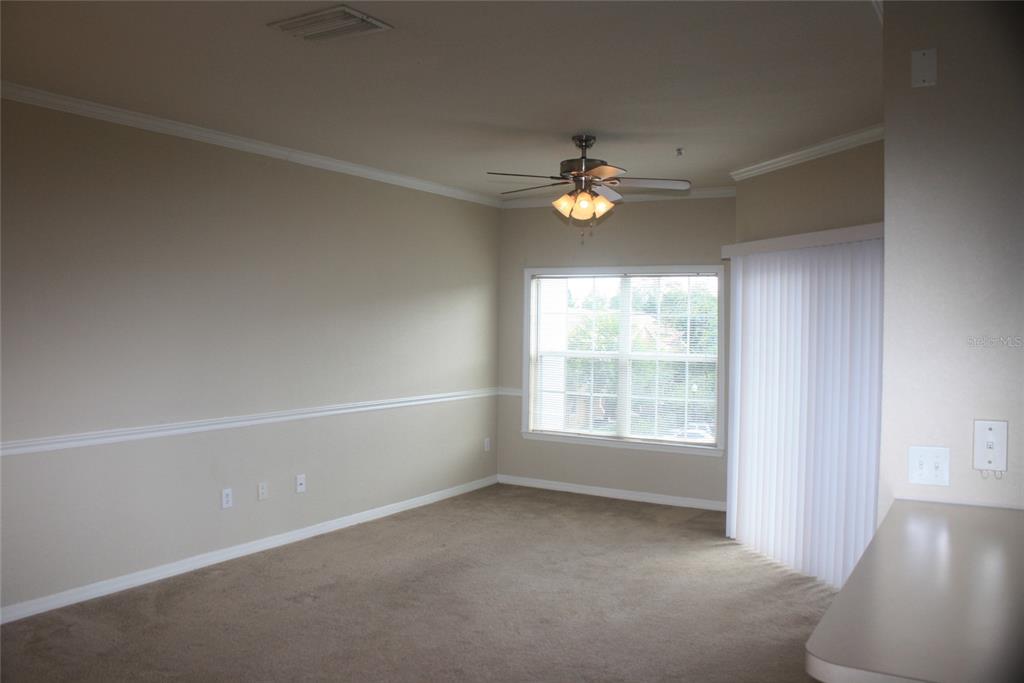 An empty living room features beige walls, a ceiling fan, carpeted floors, and a sliding door — 3621 CONROY ROAD UNIT 739, ORLANDO, FL