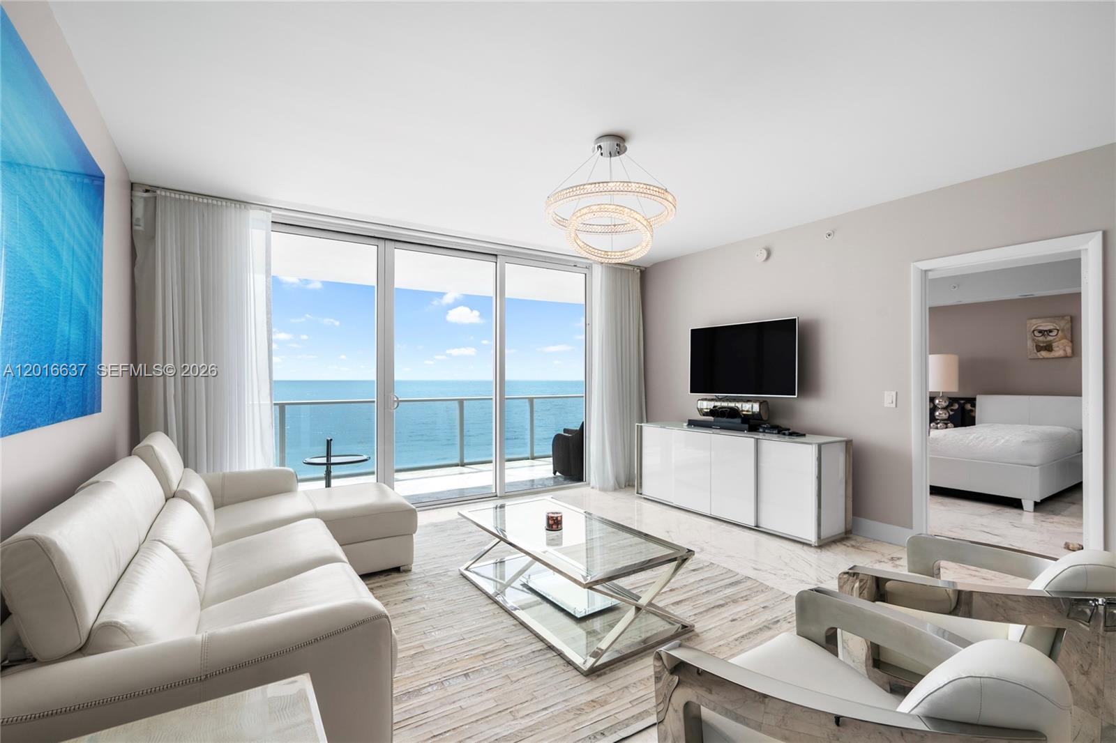 A modern living room features white leather furniture, a glass coffee table, and ocean views — 3951 S Ocean Dr # 1002, Hollywood FL 33019, HOLLYWOOD, FL