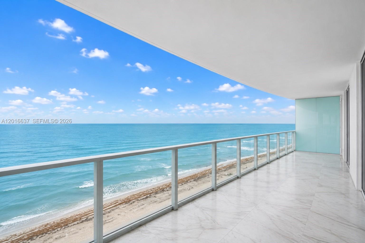 A balcony with white marble flooring and a glass railing overlooks the ocean — 3951 S Ocean Dr # 1002, Hollywood FL 33019, HOLLYWOOD, FL