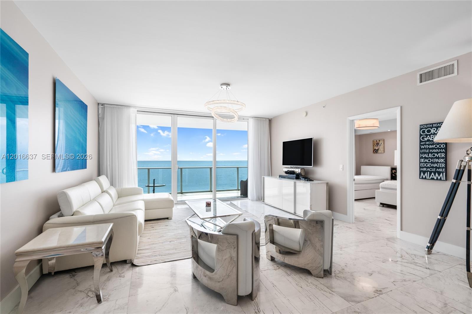 A modern living room features white leather furniture, marble floors, and a balcony overlooking the ocean — 3951 S Ocean Dr # 1002, Hollywood FL 33019, HOLLYWOOD, FL