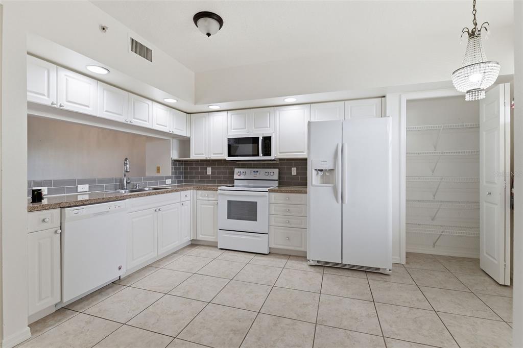 A kitchen features white cabinets, stainless steel appliances, gray subway tile backsplash, and tile flooring — 960 STARKEY ROAD UNIT 2403, LARGO, FL