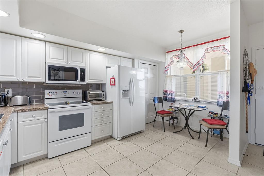 A kitchen with white cabinets, stainless steel appliances, and a small dining area by a window — 960 STARKEY ROAD UNIT 2403, LARGO, FL