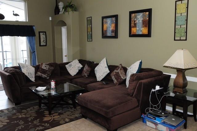 A living room features a large brown sectional sofa, a glass coffee table, and wall art — 8015 INDIAN CREEK BOULEVARD, KISSIMMEE, FL