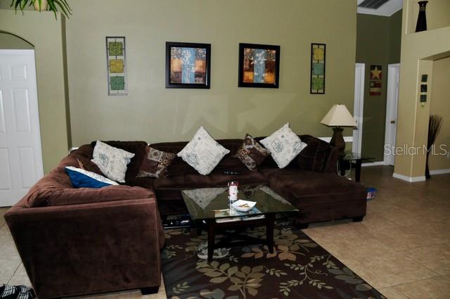 A brown sectional sofa sits on a patterned rug in a living room with green walls — 8015 INDIAN CREEK BOULEVARD, KISSIMMEE, FL