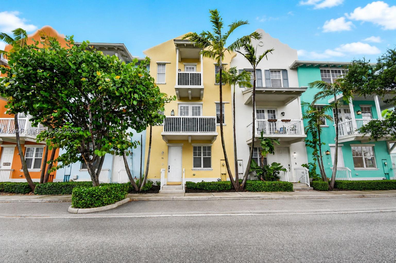 A row of colorful three-story townhouses features balconies, palm trees, and a paved street — 810 N 3rd Ave N # 76, Lake Worth FL 33460, LAKE WORTH, FL