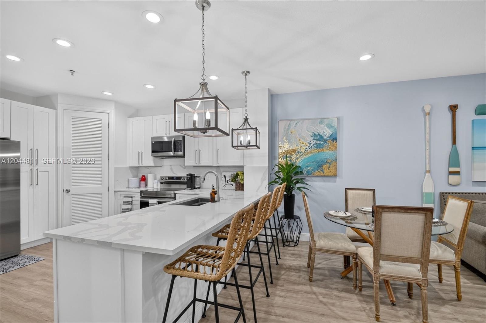 A modern kitchen features white cabinetry, a marble-topped island with bar stools, and dining area — 810 N 3rd Ave N # 76, Lake Worth FL 33460, LAKE WORTH, FL