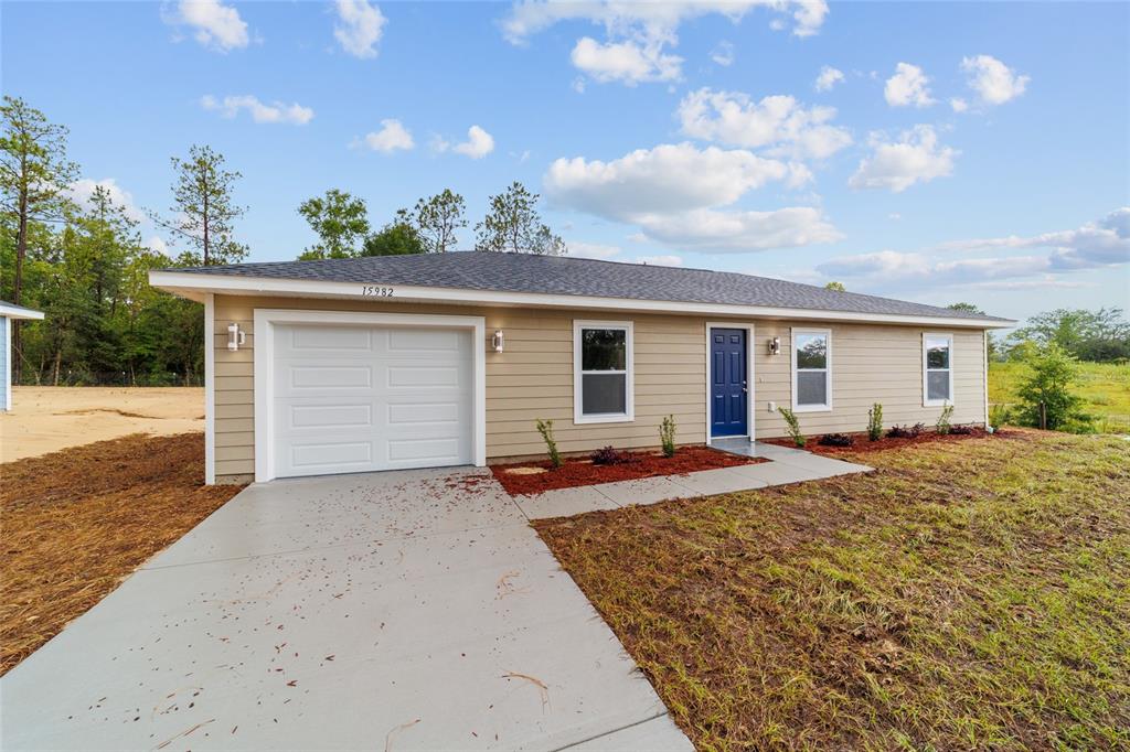 A single-story house with tan siding, a blue front door, and a concrete driveway — 15776 SW 27TH LANE, OCALA, FL