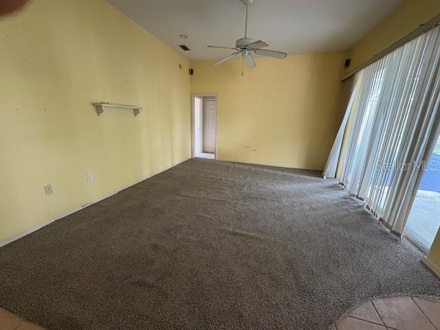 A living room with yellow walls, gray carpeting, a ceiling fan, and sliding glass doors — 711 128TH STREET NE, BRADENTON, FL