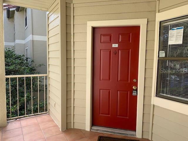 A red front door with a keypad lock is situated on a tiled balcony — 3016 PARKWAY BOULEVARD UNIT 204, KISSIMMEE, FL