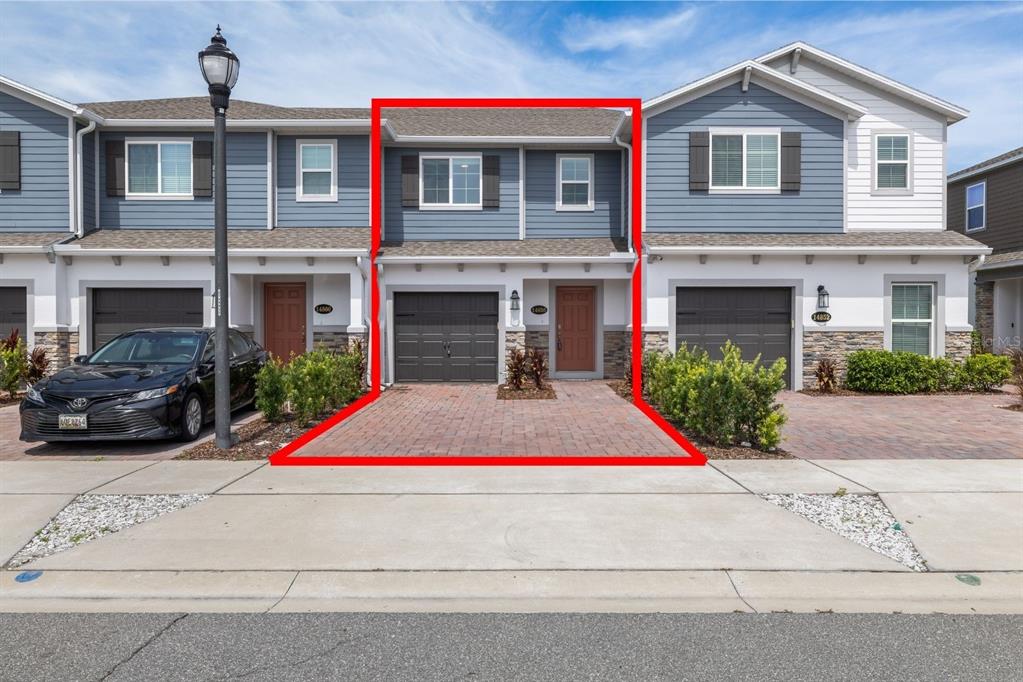 A two-story townhouse with a brick driveway, dark garage door, and blue siding — 14856 HARVEST STREET, ORLANDO, FL