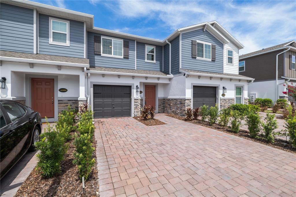 A two-story townhouse exterior features blue siding, stone accents, and a brick paver driveway — 14856 HARVEST STREET, ORLANDO, FL