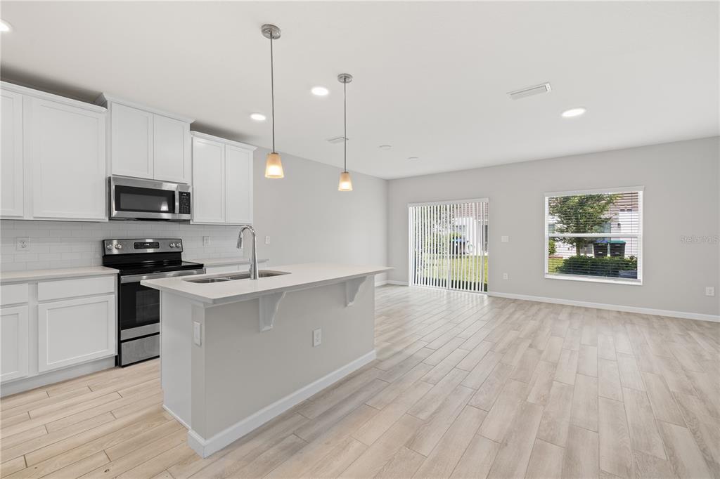 A kitchen with white cabinets, a central island, and light wood-look flooring — 14856 HARVEST STREET, ORLANDO, FL