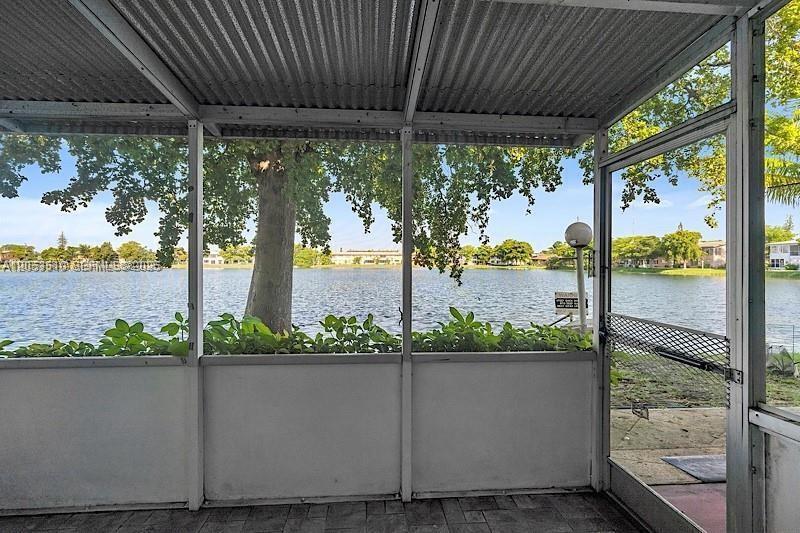 A screened-in patio overlooks a lake with a tree and residential buildings in the distance — 19000 NE 3rd Ct # 405, Miami FL 33179, MIAMI, FL
