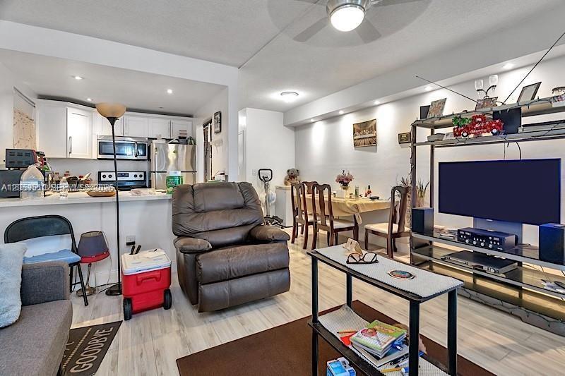 An open-concept living room features a recliner, a dining area, and a kitchen with white cabinets — 19000 NE 3rd Ct # 405, Miami FL 33179, MIAMI, FL