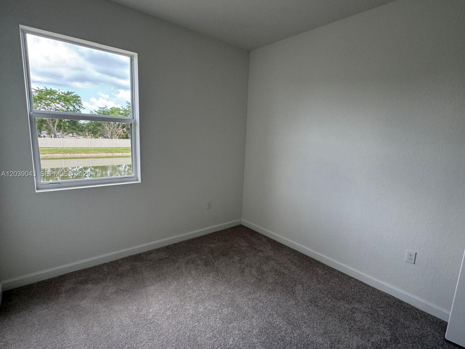 An empty bedroom features gray carpet, white walls, and a window overlooking a pond — 18402 SW 2nd St, Pembroke Pines FL 33029, PEMBROKE PINES, FL